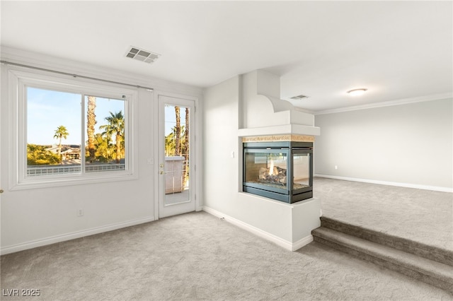 unfurnished living room with a multi sided fireplace, visible vents, baseboards, and carpet