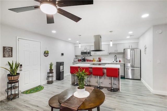 kitchen with a center island, appliances with stainless steel finishes, island range hood, light wood finished floors, and light countertops