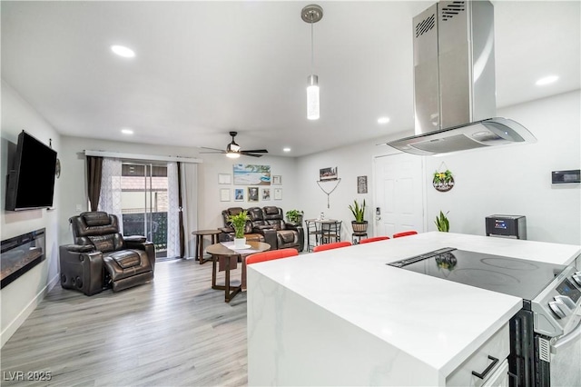 kitchen with electric stove, range hood, light wood finished floors, light countertops, and hanging light fixtures