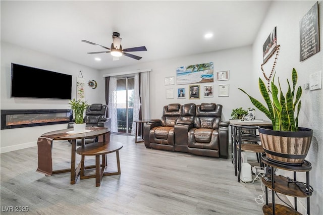 living room featuring light wood-type flooring, a glass covered fireplace, recessed lighting, baseboards, and ceiling fan