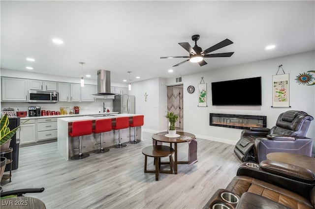 living room featuring a ceiling fan, baseboards, light wood-style flooring, recessed lighting, and a glass covered fireplace