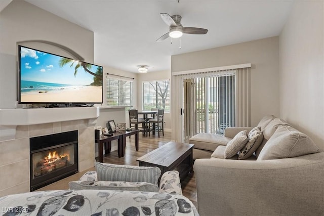 living room with a tiled fireplace, a ceiling fan, and wood finished floors