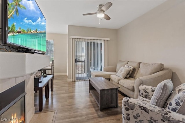 living area with a tiled fireplace, wood finished floors, baseboards, and a ceiling fan