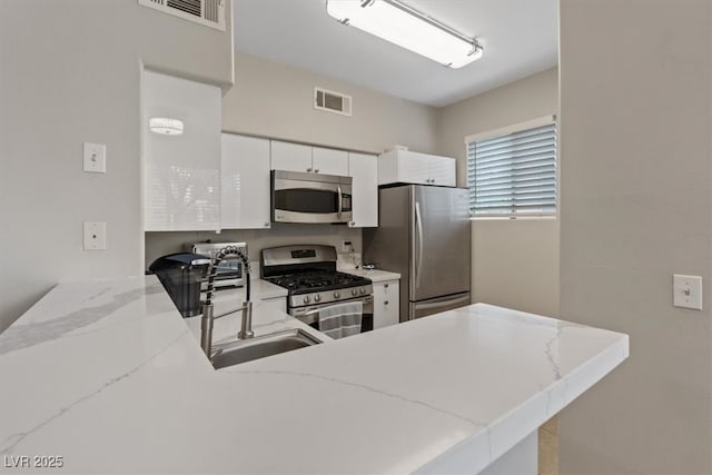 kitchen with stainless steel appliances, visible vents, a peninsula, and white cabinets