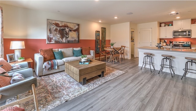 living room featuring light wood finished floors, visible vents, and recessed lighting