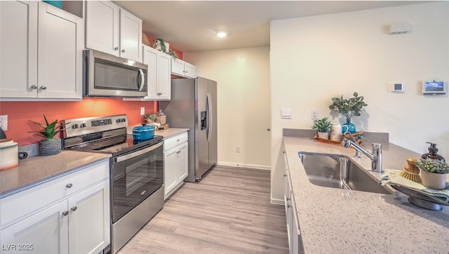 kitchen featuring light stone counters, light wood-style flooring, stainless steel appliances, white cabinetry, and a sink