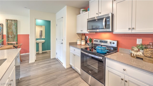 kitchen with light wood finished floors, appliances with stainless steel finishes, white cabinetry, and light stone countertops