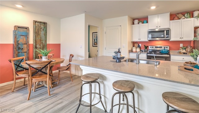 kitchen featuring a breakfast bar area, light stone counters, appliances with stainless steel finishes, white cabinetry, and a sink