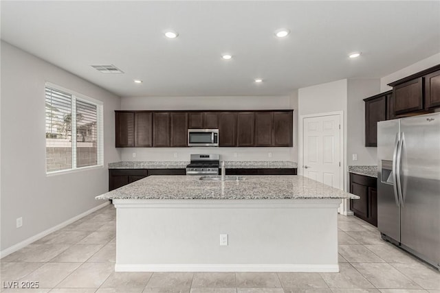 kitchen featuring light stone countertops, visible vents, a kitchen island with sink, dark brown cabinets, and appliances with stainless steel finishes