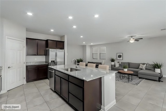 kitchen with dark brown cabinets, an island with sink, light stone counters, stainless steel appliances, and a sink