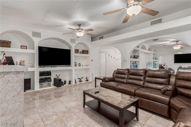 living room featuring built in shelves, arched walkways, visible vents, and a textured ceiling