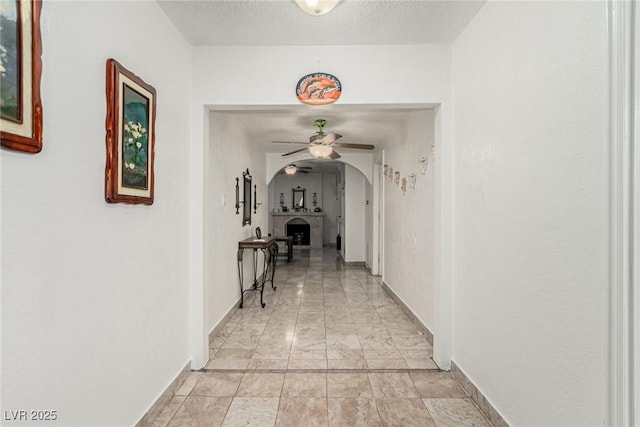 corridor featuring baseboards, arched walkways, and a textured ceiling