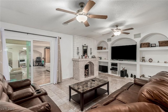 living area featuring built in features, a ceiling fan, a textured ceiling, marble finish floor, and a large fireplace