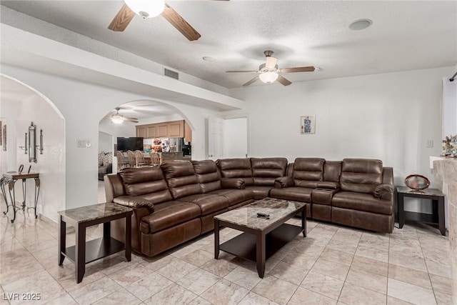 living area featuring arched walkways, visible vents, a textured ceiling, and a ceiling fan