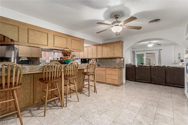 kitchen featuring visible vents, a breakfast bar, arched walkways, fridge, and tasteful backsplash