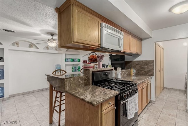 kitchen featuring stainless steel gas range oven, visible vents, a breakfast bar, a peninsula, and white microwave