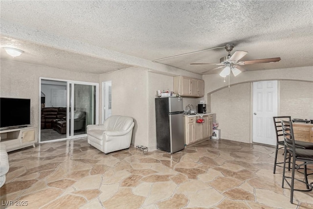 kitchen featuring a ceiling fan, a textured ceiling, freestanding refrigerator, arched walkways, and light countertops