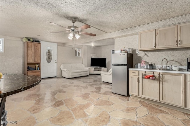 kitchen featuring light brown cabinets, freestanding refrigerator, ceiling fan, a sink, and a textured ceiling