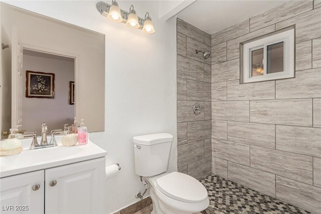 bathroom with a tile shower, toilet, vanity, and baseboards