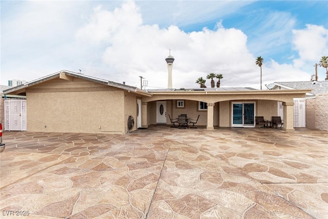 back of house with outdoor dining space, stucco siding, solar panels, and a patio