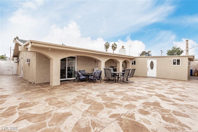 rear view of house with outdoor dining space, stucco siding, and a patio