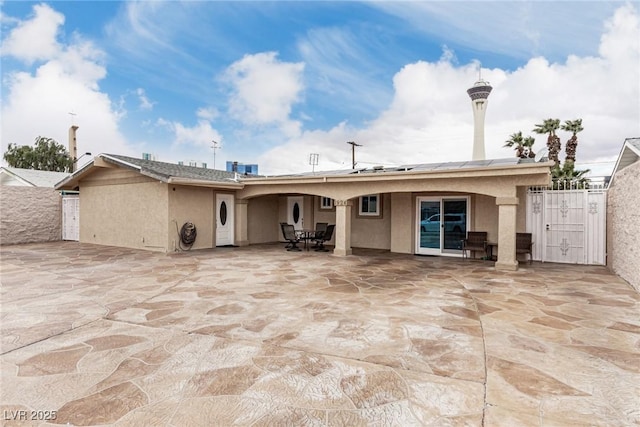 rear view of property with solar panels, a patio area, fence, and stucco siding