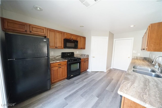 kitchen featuring visible vents, light wood-style flooring, a sink, black appliances, and light countertops