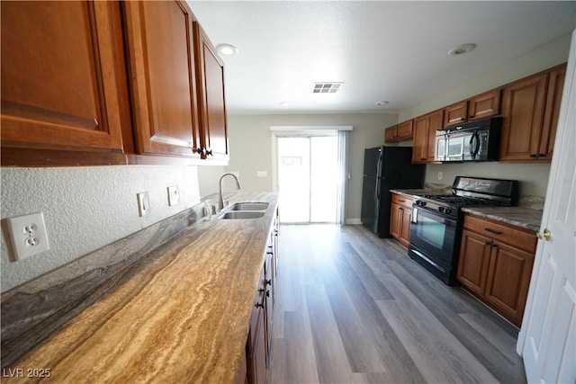 kitchen with visible vents, brown cabinets, black appliances, a sink, and wood finished floors