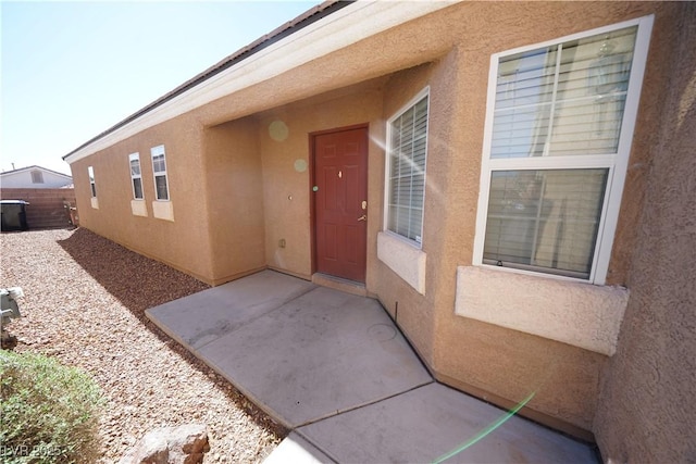 entrance to property featuring stucco siding, a patio, and fence