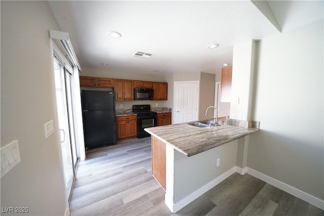 kitchen with visible vents, a peninsula, brown cabinetry, black appliances, and a sink