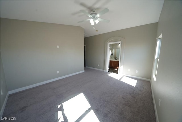 unfurnished bedroom featuring lofted ceiling, a ceiling fan, ensuite bathroom, carpet flooring, and baseboards