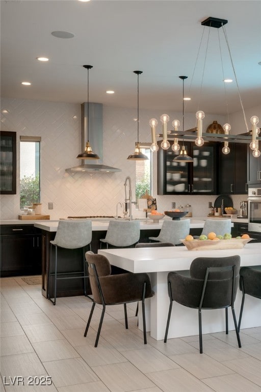 kitchen with stainless steel oven, a kitchen bar, wall chimney exhaust hood, and light countertops