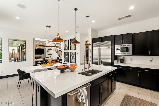 kitchen with visible vents, a sink, decorative backsplash, built in appliances, and dark cabinets