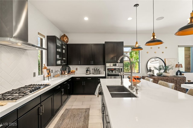 kitchen featuring appliances with stainless steel finishes, light countertops, wall chimney exhaust hood, and a sink