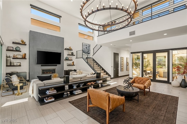 living room with a wealth of natural light, french doors, a notable chandelier, and a glass covered fireplace