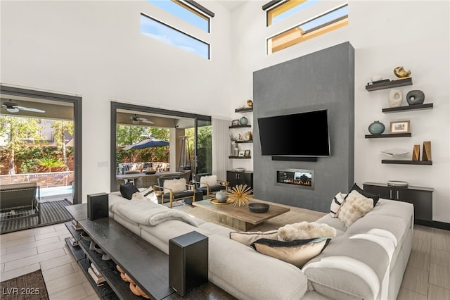 living area with a glass covered fireplace, a high ceiling, plenty of natural light, and wood finished floors