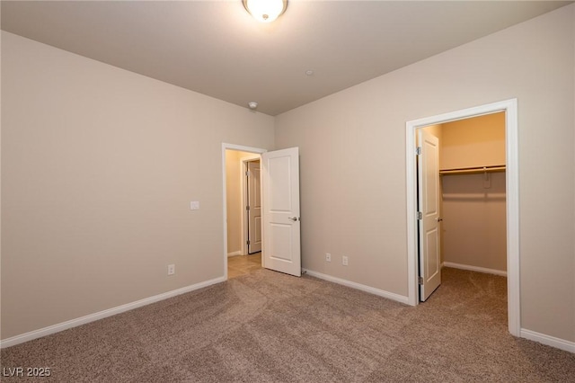 unfurnished bedroom with a closet, baseboards, a spacious closet, and carpet flooring