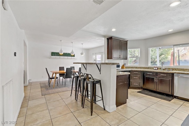 kitchen featuring dark brown cabinetry, a kitchen breakfast bar, light tile patterned flooring, and stainless steel dishwasher