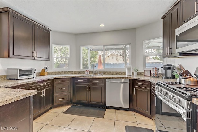 kitchen with a sink, light stone counters, dark brown cabinetry, appliances with stainless steel finishes, and a toaster