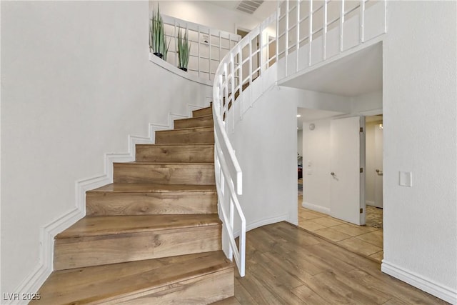 stairway featuring a high ceiling, wood finished floors, visible vents, and baseboards