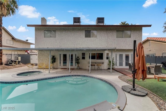 rear view of property with fence, stucco siding, french doors, a patio area, and an in ground hot tub