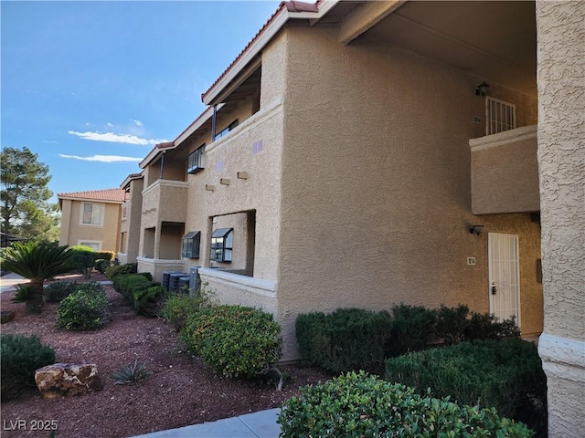 view of side of home featuring a tile roof, cooling unit, and stucco siding