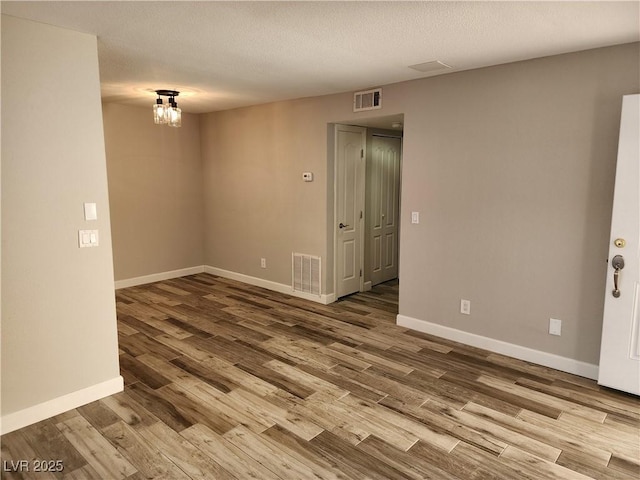 unfurnished room featuring a textured ceiling, wood finished floors, visible vents, and baseboards