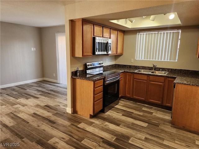 kitchen with brown cabinetry, appliances with stainless steel finishes, dark wood-style floors, a raised ceiling, and a sink