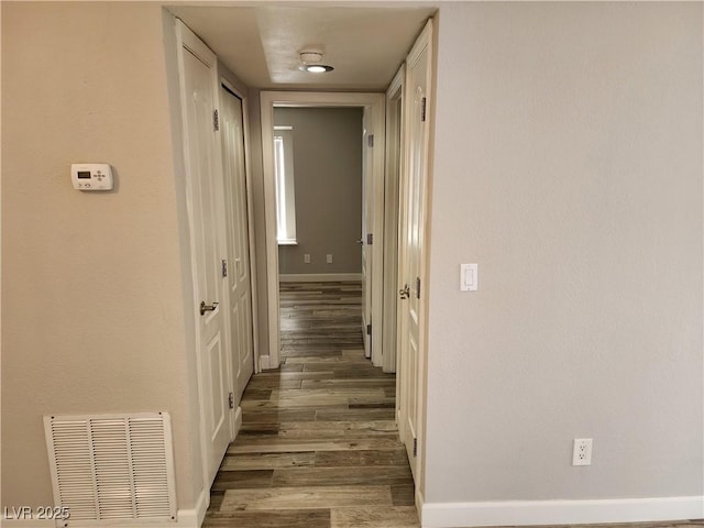 corridor featuring visible vents, baseboards, and wood finished floors