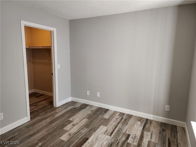 unfurnished bedroom featuring a walk in closet, baseboards, a closet, and wood finished floors