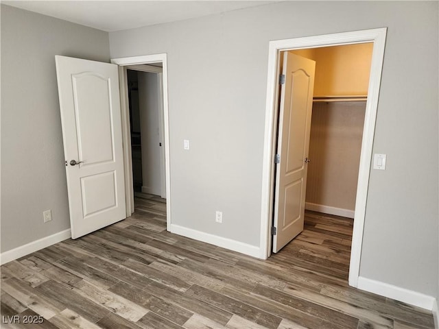 unfurnished bedroom featuring a closet, a walk in closet, baseboards, and wood finished floors