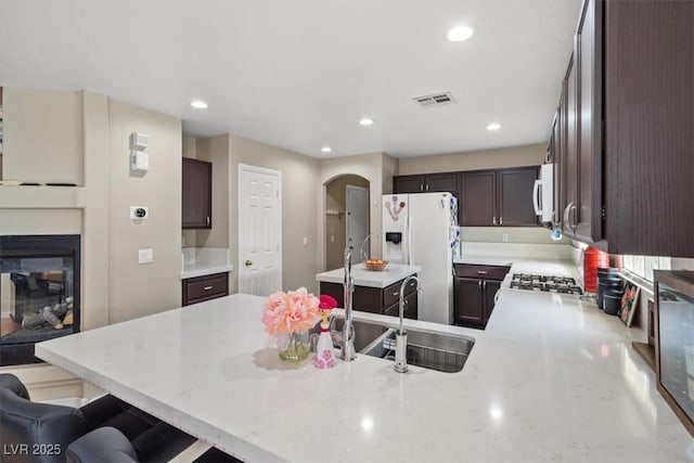 kitchen featuring white appliances, visible vents, a peninsula, arched walkways, and dark brown cabinets