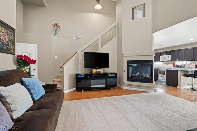 living room with light wood-style flooring, baseboards, a towering ceiling, and stairs