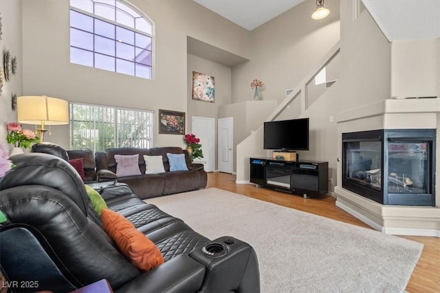 living area featuring a high ceiling, wood finished floors, and a multi sided fireplace